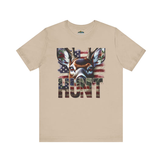 A beige t-shirt with a graphic of an eagle and an American flag, overlaying bold letters spelling "hunt" across the chest. The design features rustic themes and celebrates hunting heritage.