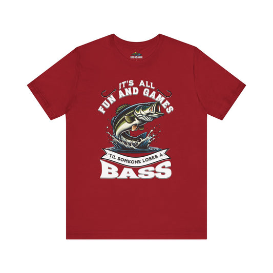 Red unisex fishing tee with a graphic showing a cartoon fish leaping out of water and the words "It's All Fun and Games Until Someone Loses a Bass" in bold text.