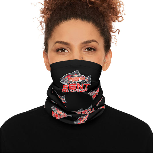 A woman with curly hair wears a Bent On Chrome - Lightweight Neck Gaiter - Red Salmon Logo Black with red and white graphics, including text and a stylized image of a snowmobile. She looks directly at the viewer, dressed in a.