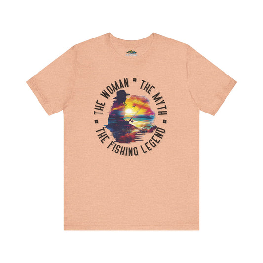 Sentence with product name: Pink unisex The Woman, The Myth, The Fishing Legend - Sunrise Silhouette - T-Shirt with a circular graphic showing a silhouette of a woman angler fishing at sunrise. Text says "The woman, the myth, the fishing legend" in bold letters around the design.