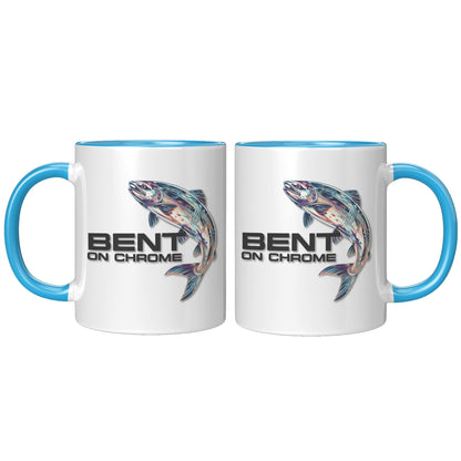 Two white Bent on Chrome - Chrome Salmon accent mugs with blue handles, each featuring a colorful illustration of a fish and the text "bent on chrome" on their surfaces. The mugs are positioned facing each other and feature