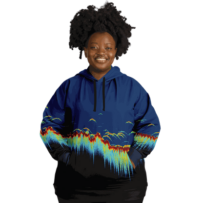 A person wearing a Sonar Scan Plus-size Hoodie, featuring vibrant abstract wave patterns, stands smiling against a black background. Their curly hair complements the playful design, exuding a cheerful demeanor that makes this piece an ideal addition to any fishing wardrobe.