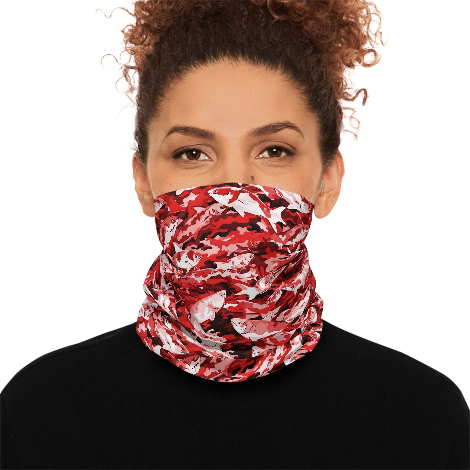 A woman with curly hair wears a Salmon Slayer - Lightweight Neck Gaiter in a fish camo pattern covering her neck and lower face. She is dressed in a black top and looks directly at the