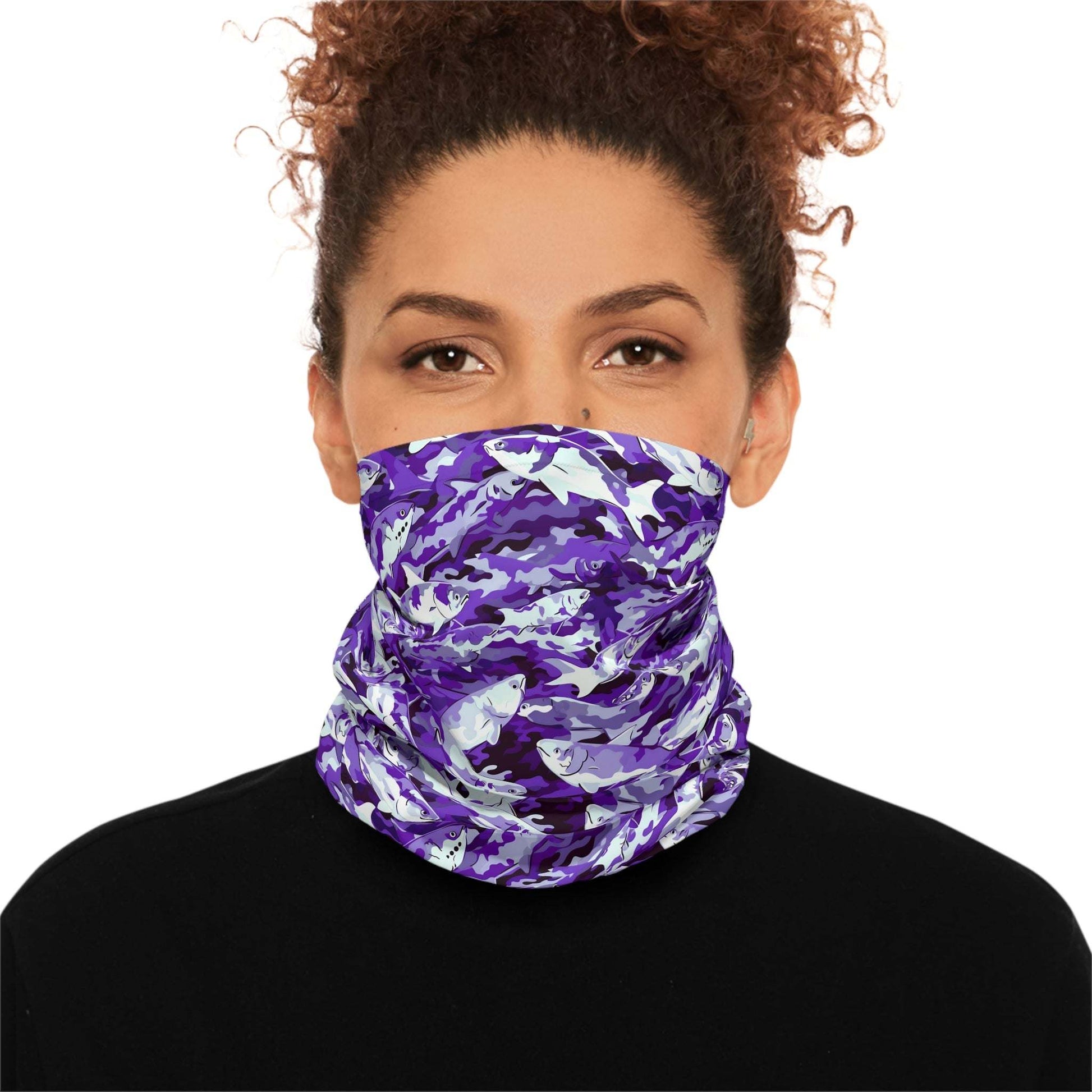 A woman with curly hair wears a Salmon Slayer - Lightweight Neck Gaiter in a fish camo pattern covering her neck and lower face. She is dressed in a black top and looks directly at the