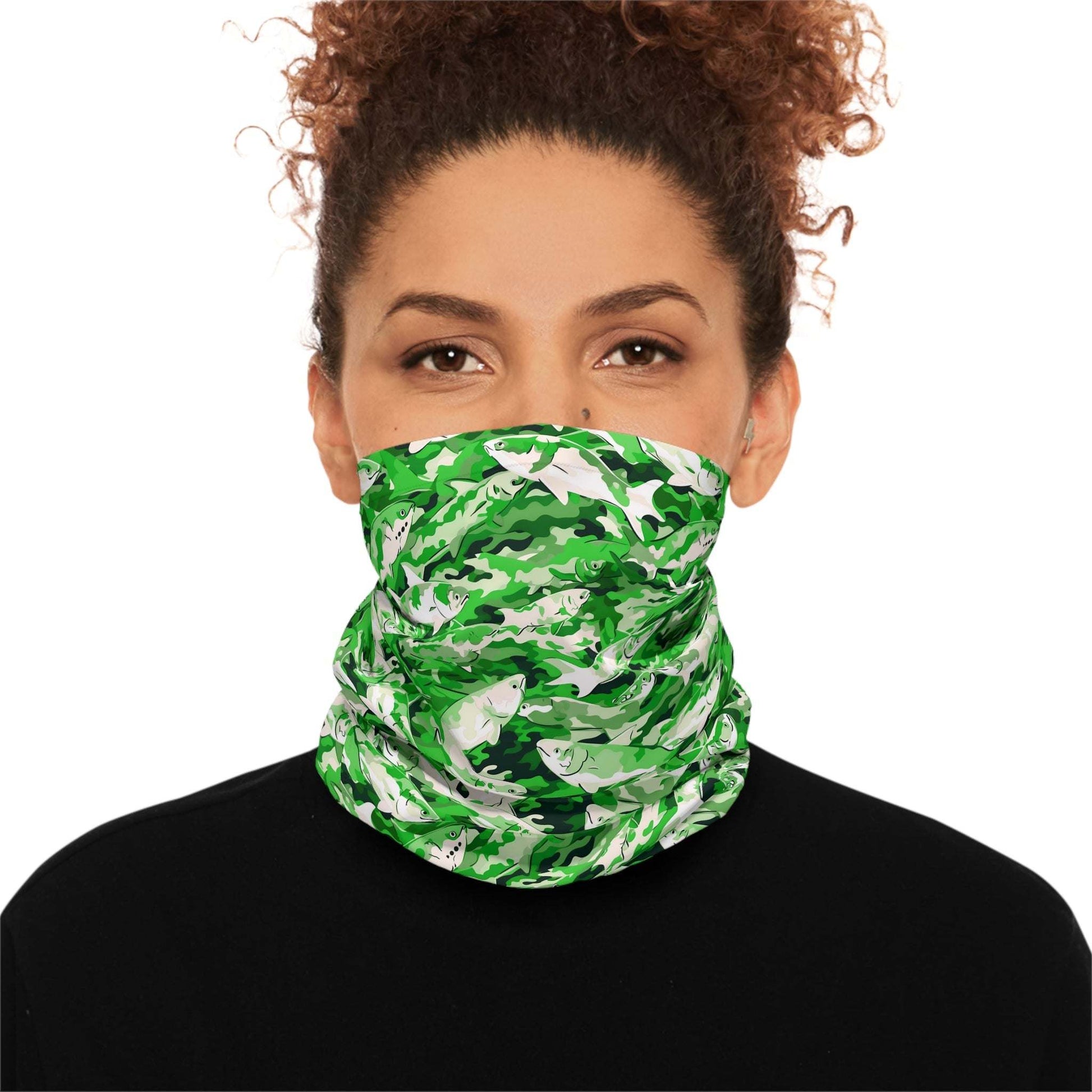 A woman with curly hair wears a Salmon Slayer - Lightweight Neck Gaiter in a fish camo pattern covering her neck and lower face. She is dressed in a black top and looks directly at the