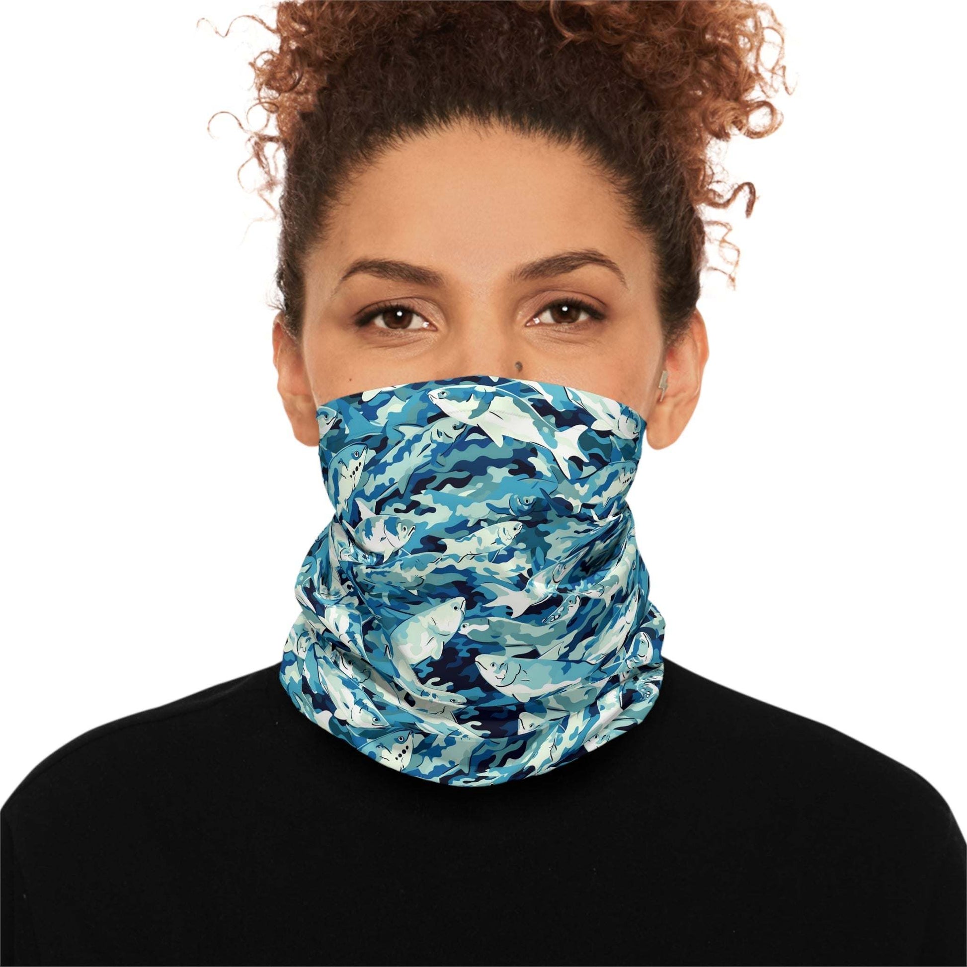 A woman with curly hair wears a Salmon Slayer - Lightweight Neck Gaiter in a fish camo pattern covering her neck and lower face. She is dressed in a black top and looks directly at the